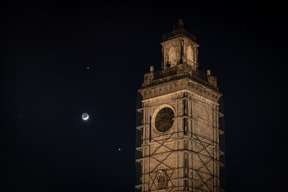 Venus and Jupiter planets in conjunction with a crescent moon rise behind municipality tower in Piazza Palazzo square in LAquila (Italy) on February 22, 2023.