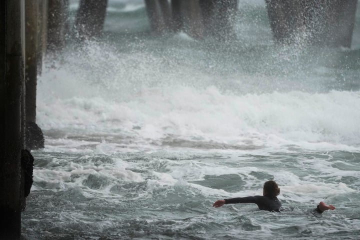 A surfer swam out into the waves under the Huntington Beach Pier on Friday. California and other parts of the West faced heavy snow and rain on Friday from the latest winter storm to hit the United States.