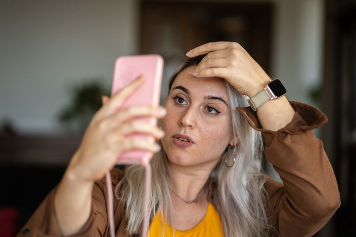 Blonde woman mirroring herself using mobile screen at home