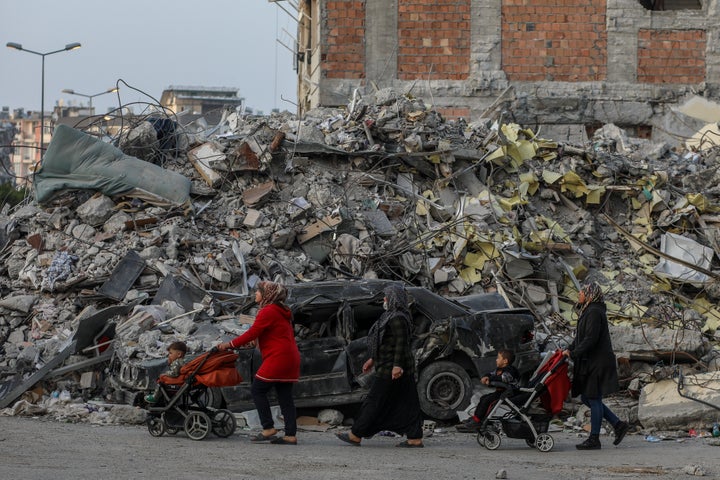 Women push children in strollers past a destroyed building on February 28, 2023, in Iskenderun, Turkey.