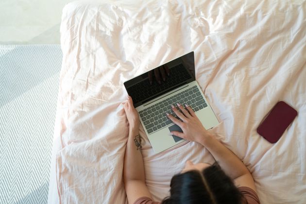 Unrecognizable woman typing on laptop while lying in bed
