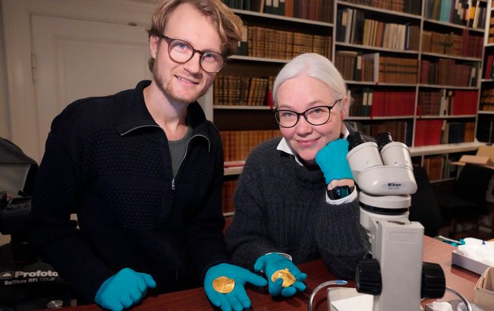 Οι ρουνολόγοι Kρίστερ Βάσχους, αριστερά, και Λίσμπετ Iμερ κρατούν χρυσά βρακτικά που ανακαλύφθηκαν στο Βίντελεβ της Δανίας στα τέλη του 2020.