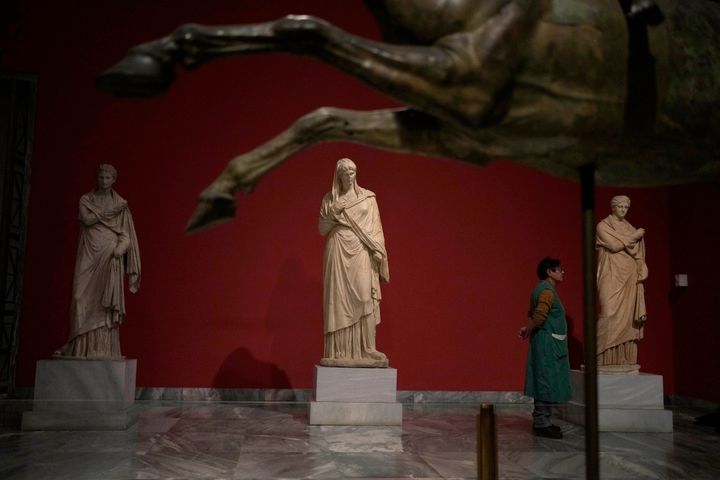 A cleaning woman stands between statues as she watches the presentation event for the planned renovation of the National Archaeological Museum in Athens, Greece, on Wednesday, Feb. 15, 2023. The British architect, David Chipperfield, is leading the project that will expand the museum's exhibition space, create a new entrance, and garden space. The museum, which showcases artifacts from ancient Greece, is considered to be one of the most important in the world. (AP Photo/Thanassis Stavrakis)