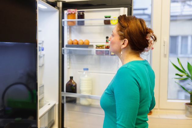 Woman standing by the open fridge and looking inside for food at meal time