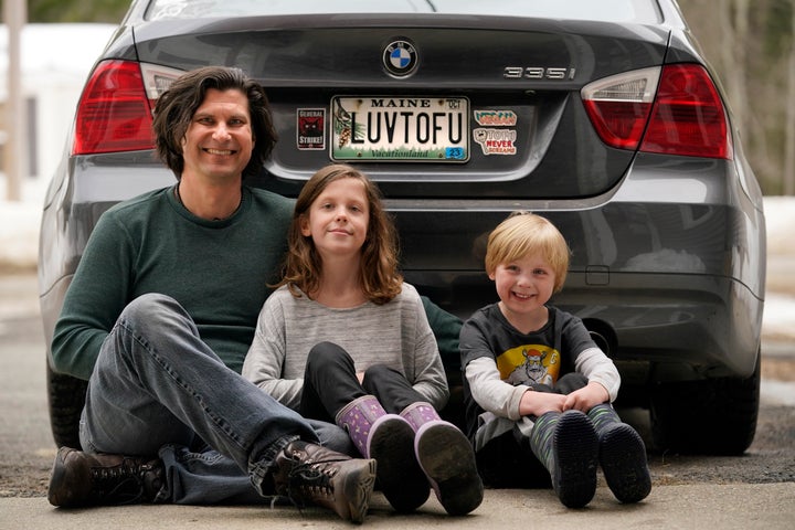 Peter Starostecki and his kids Sadie, center, and Jo Jo, pose behind their car with the vanity license plate that the state of Maine has deemed in appropriate, Wednesday, March 8, 2023, in Poland, Maine. The vegan family's car will soon have a randomly selected plate. (AP Photo/Robert F. Bukaty)