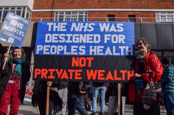 Protesters hold a banner which states 'The NHS was designed for people's health, not private wealth' during the demonstration.