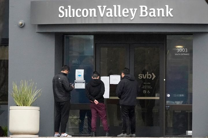 People look at signs posted outside of an entrance to Silicon Valley Bank in Santa Clara, Calif., Friday, March 10, 2023. From winemakers in California to startups across the Atlantic Ocean, companies are scrambling to figure out how to manage their finances after their bank, Silicon Valley Bank, suddenly shut down on Friday. The meltdown means distress not only for businesses but also for all their workers whose paychecks may get tied up in the chaos. 