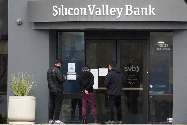 People look at signs posted outside of an entrance to Silicon Valley Bank in Santa Clara, Calif., Friday, March 10, 2023. From winemakers in California to startups across the Atlantic Ocean, companies are scrambling to figure out how to manage their finances after their bank, Silicon Valley Bank, suddenly shut down on Friday. The meltdown means distress not only for businesses but also for all their workers whose paychecks may get tied up in the chaos.