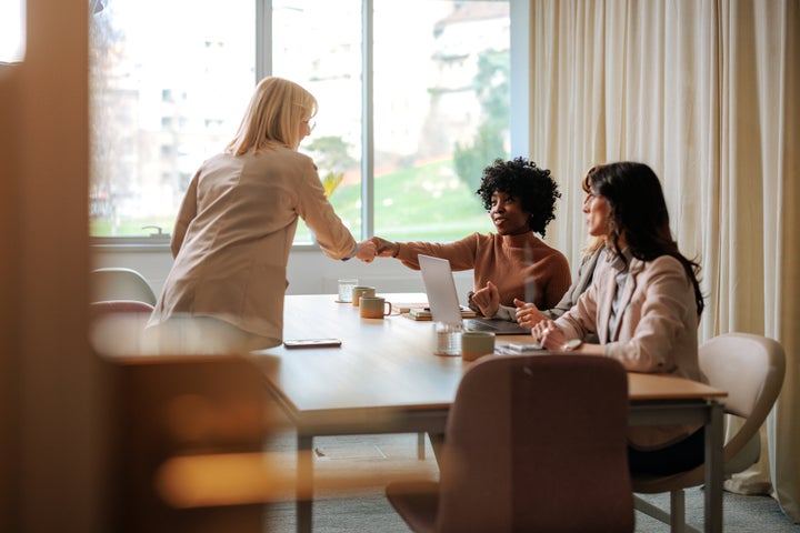 A young job candidate is in an office shaking hands with the HR team during introductions.