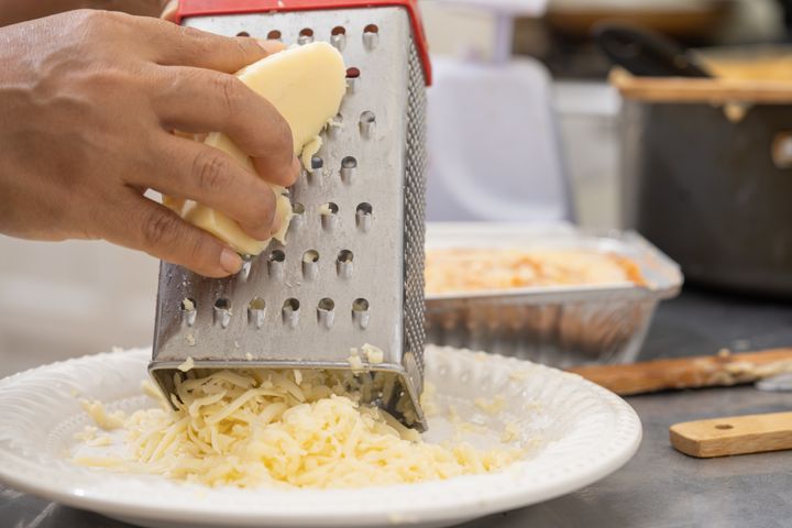 Hands using metal grater for mozzarella cheese in lasagna