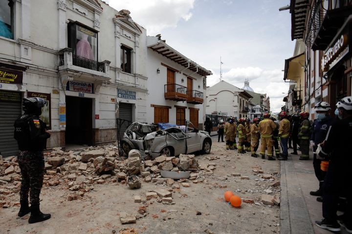 Rescue workers stand next to a car crushed by debris following an earthquake in Cuenca, Ecuador, Saturday March 18, 2023.  The US Geological Survey reported a magnitude 6.7 earthquake about 50 miles south of Guayaquil.  (AP Photo/Xavier Caivinagua)