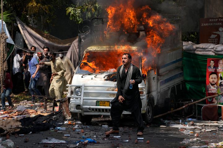 Supporters of former Prime Minister Imran Khan throw stones toward police next a burning vehicle during clashes, in Lahore, Pakistan, Wednesday, March 15, 2023.(AP Photo/K.M. Chaudary)