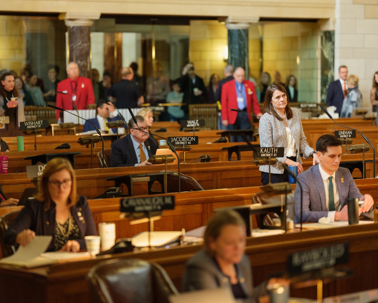 Nebraska state Sens. Machaela Cavanaugh (seated, left) and Kathleen Kauth (standing, right) are on opposite ends of the debate over gender-affirming treatment for trans youth.