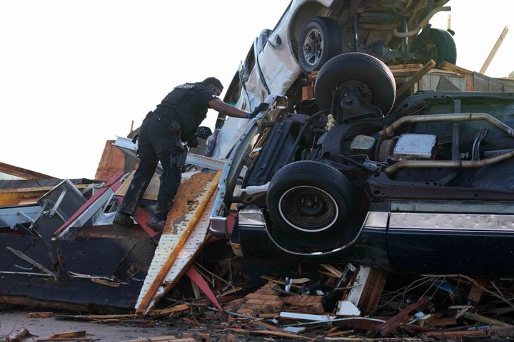 A sheriff's deputy climbs onto a pile of wind-tossed vehicles to search for survivors or the deceased at Chuck's Dairy Bar in Rolling Fork, Miss., Saturday, March 25, 2023. Emergency officials in Mississippi say several people have been killed by tornadoes that tore through the state on Friday night, destroying buildings and knocking out power as severe weather produced hail the size of golf balls moved through several southern states.