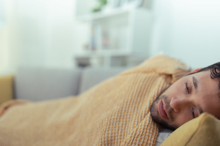 Young man, lying on the couch in the living room, covered with a yellow blanket, very cold and with fever.