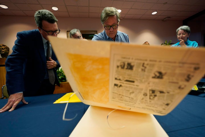 Peter Mangan, center, and his wife, Karen, right, look through a large folder of newspaper clippings at the Lyndon B. Johnson's presidential library with LBJ Library director Mark Lawrence, left, Wednesday, Aug. 31, 2022, in Austin, Texas. The family of late Associated Press reporter James W. Mangan has donated to the library cassette tapes containing interviews the reporter did that led to a 1977 story in which a Texas voting official detailed how three decades earlier, votes were falsified to give Johnson a slim victory in a U.S. Senate primary. (AP Photo/Eric Gay)