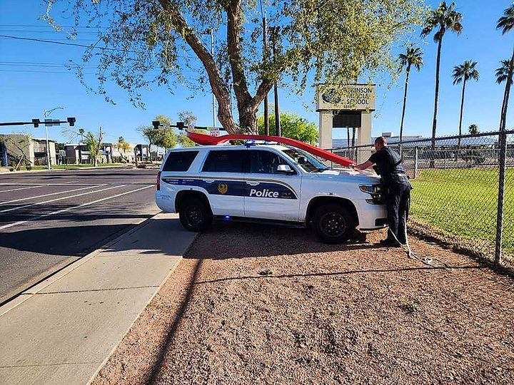 This photo provided by Michael Foster shows a Phoenix police officer strapping down a 15-foot red spoon to his police cruiser in Phoenix on Monday, April 3, 2023. Foster found the giant red spoon while playing Pokemon GO. It was stolen from an Arizona Dairy Queen on March 25 and sparked a mystery on social media. (Michael Foster via AP)