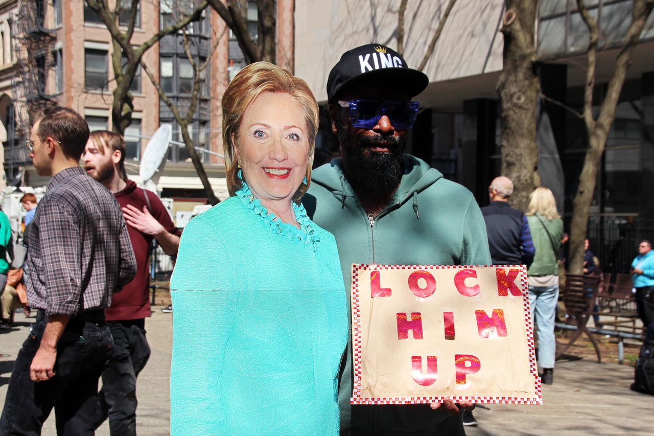 A protester holds a sign reading "Lock him up" while standing next to a photo of Clinton.