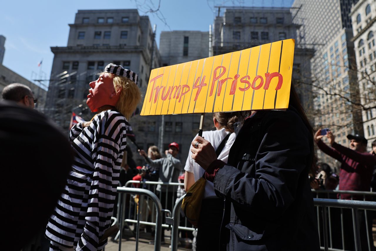 A person holds a sign reading "Trump 4 Prison."