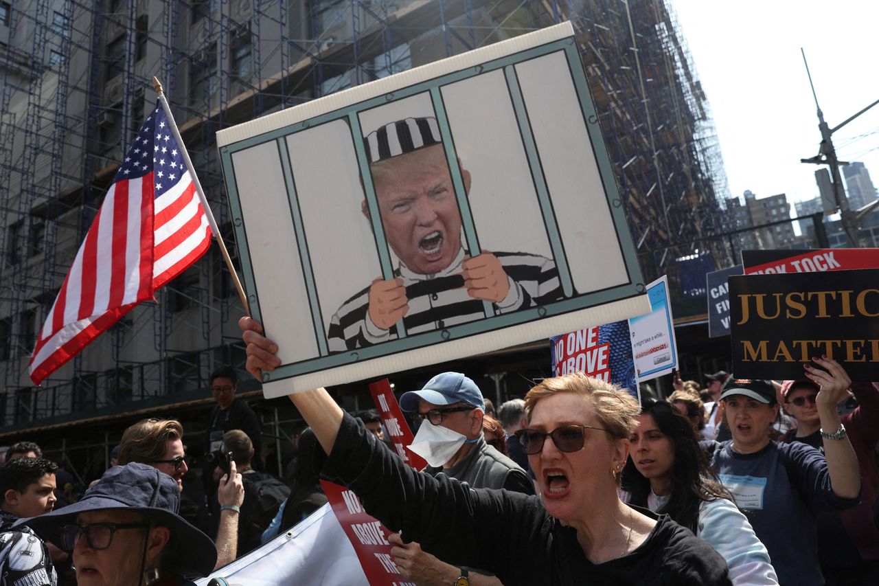 People demonstrate with a sign depicting Trump behind bars.