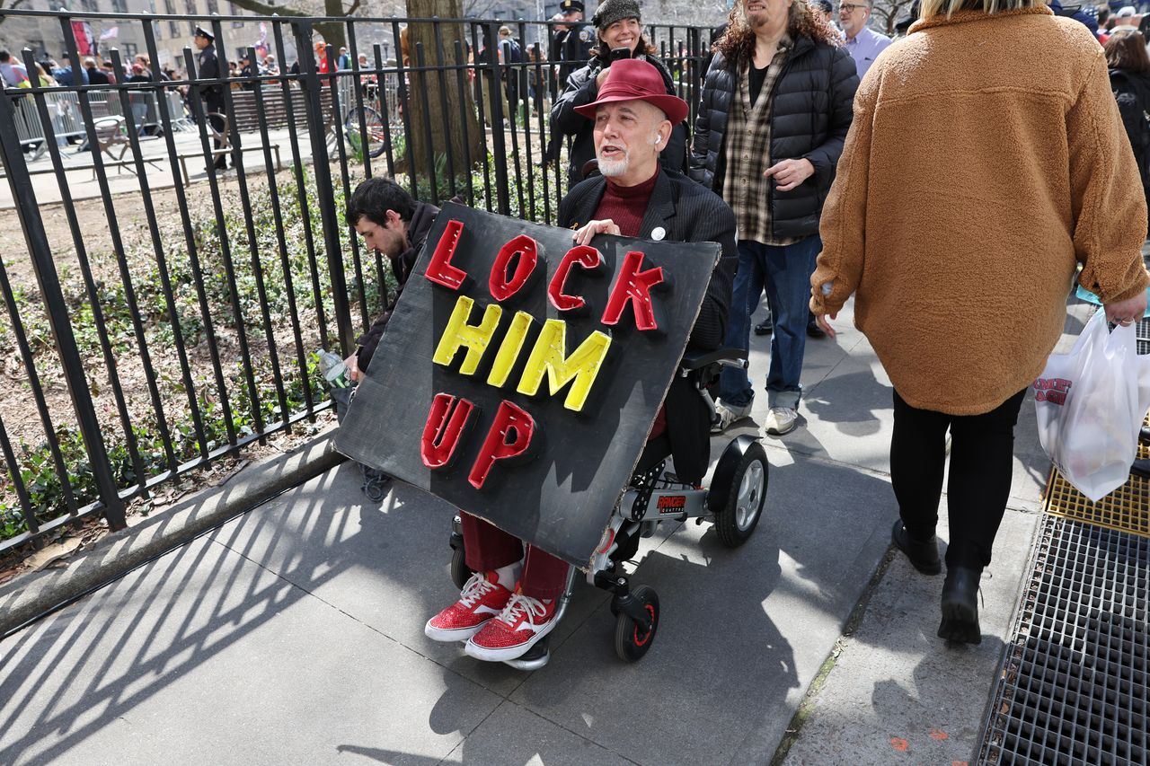 A man holds a sign reading "lock him up."