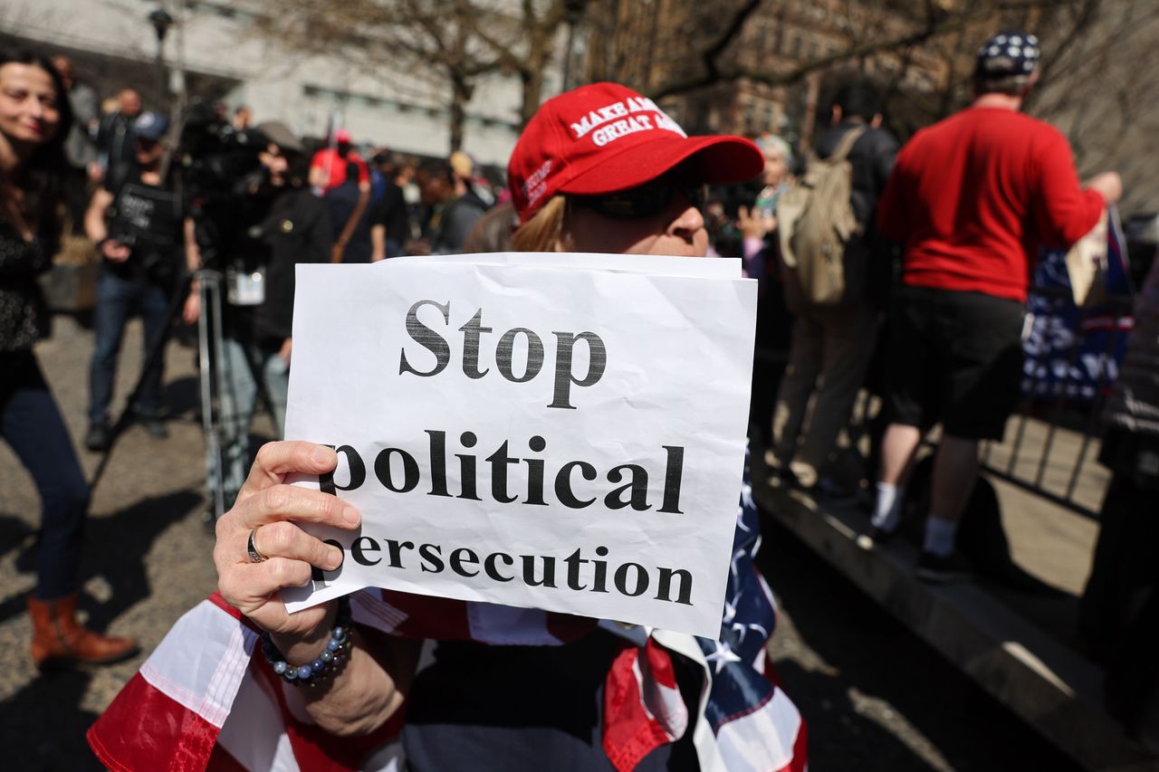 A Trump supporter holds a sign reading "stop political persecution" ahead of the arraignment.