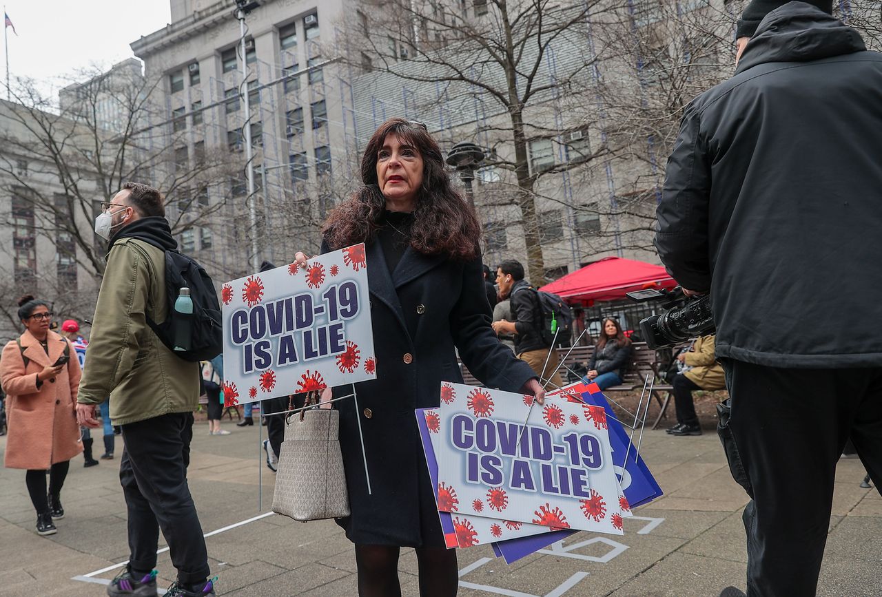 A woman holds signs that claim "COVID-19 is a lie" during protests in lower Manhattan.