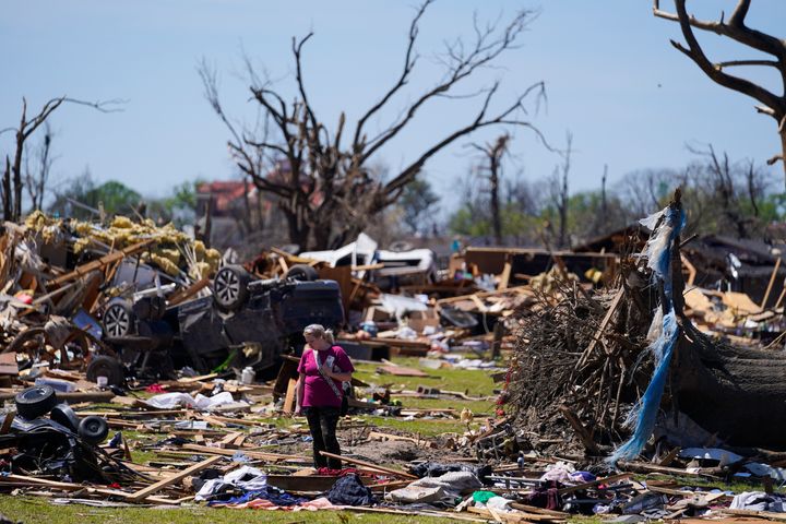 A woman walks near an uprooted tree, a flipped vehicle and debris from homes damaged by a tornado on March 27, 2023, in Rolling Fork, Miss. Gov. Tate Reeves declared a state of emergency Tuesday, April 4, in five north Mississippi counties where severe storms killed one person and damaged hundreds of homes over the weekend. 