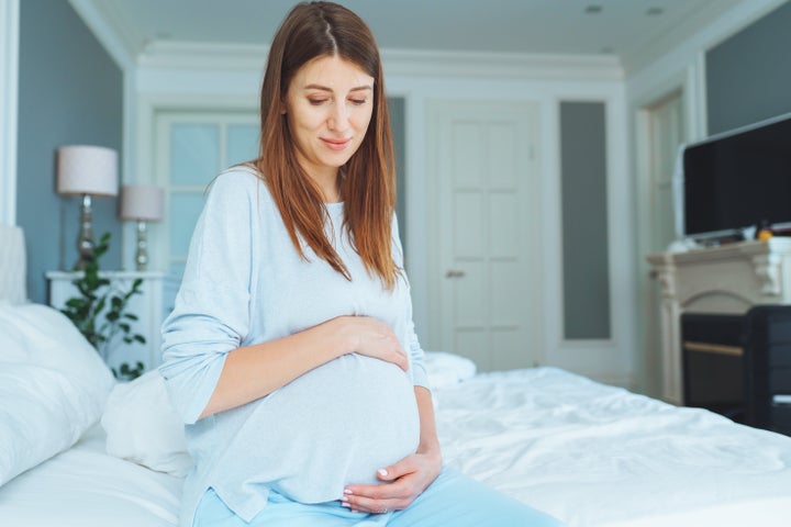 Thoughtful and relaxed pregnant surrogate mother holding and touching her abdomen, looking down