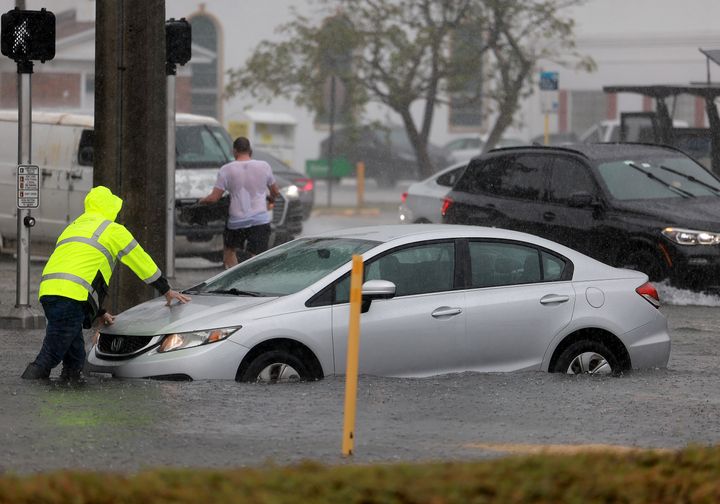 A driver pushes his stalled car through a flooded street on April 12, 2023 in Dania Beach, Florida. 