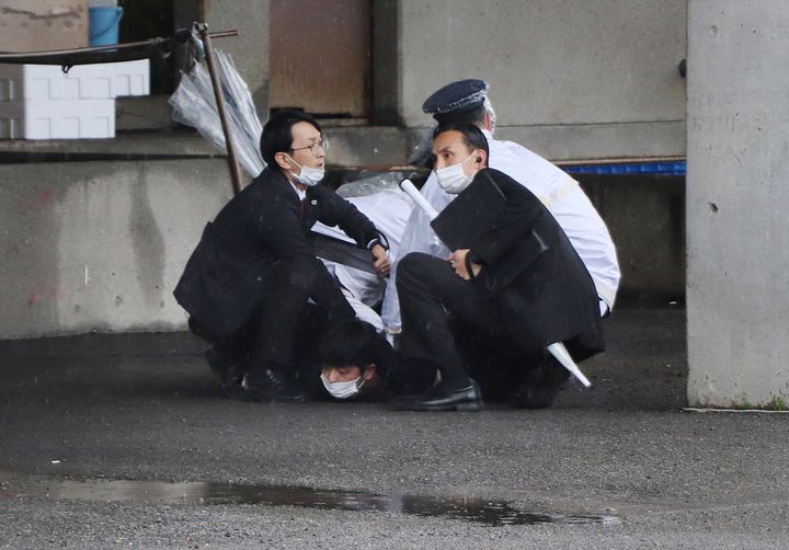 A man (bottom) is arrested after throwing what appeared to be a smoke bomb in Wakayama on April 15, 2023. - Japanese Prime Minister Fumio Kishida was evacuated from a port in Wakayama after a blast was heard, but he was unharmed in the incident, local media reported on April 15. (Photo by JIJI Press / AFP) / Japan OUT (Photo by STR/JIJI Press/AFP via Getty Images)