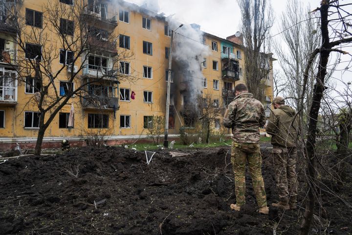 Soldiers stand next to the crater from a rocket attack by Russian troops while a residential building burns in the background in Sloviansk. 