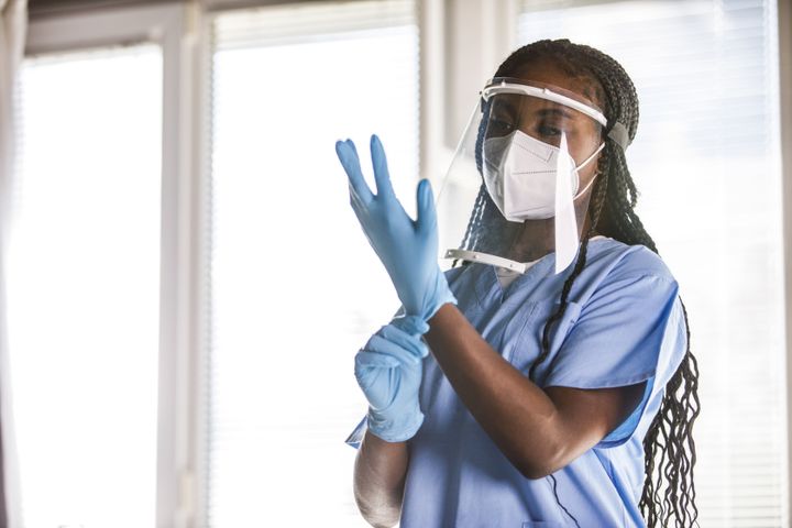  Black nurse putting on disposable protective gloves before examining a patient. Part of a series.