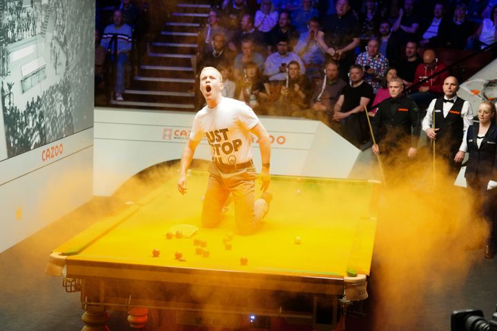A 'Just Stop Oil' protester jumps on the table and throws orange powder during the match between Robert Milkins against Joe Perry during day three of the Cazoo World Snooker Championship at the Crucible Theatre, Sheffield.