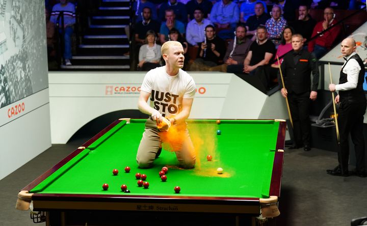 A 'Just Stop Oil' protester jumps on the table and throws orange powder during the match between Robert Milkins against Joe Perry during day three of the Cazoo World Snooker Championship at the Crucible Theatre, Sheffield.