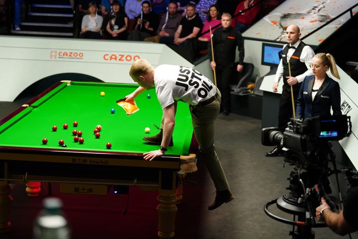 A Just Stop Oil protester jumps on the table and throws orange powder during the match between Robert Milkins against Joe Perry during day three of the Cazoo World Snooker Championship at the Crucible Theatre, Sheffield. Picture date: Monday April 17, 2023. (Photo by Mike Egerton/PA Images via Getty Images)