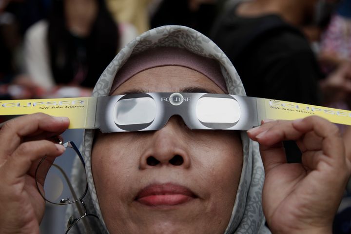 A woman uses solar eclipse glasses as they watch the hybrid solar eclipse phenomenon at Jakarta Planetarium.