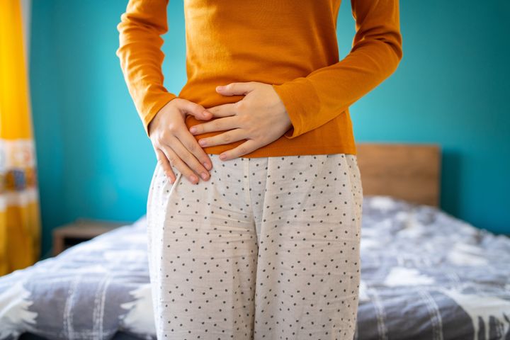 A young woman is having pain in her stomach and holding it with both hands