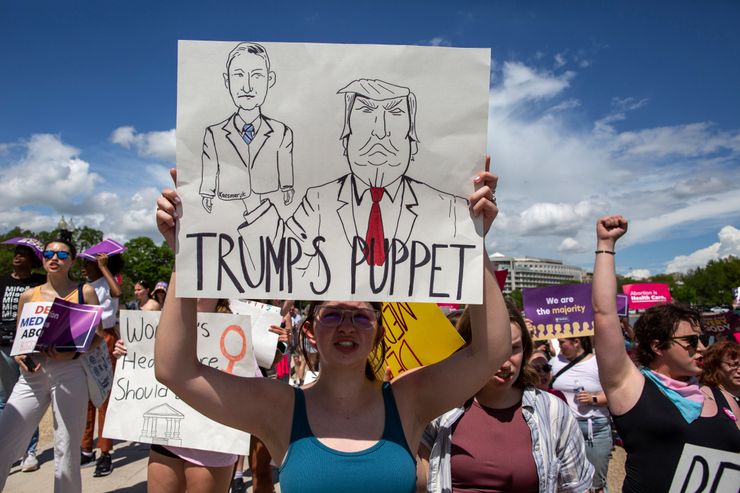 An abortion rights activist holds a sign with a sketch of Judge Matthew Kacsmaryk and former President Donald Trump, with "Trump's puppet" written on it at a rally April 14, the day the Supreme Court temporarily preserved access to mifepristone.
