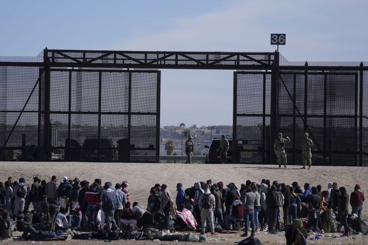 FILE - Migrants who crossed the border from Mexico into the U.S. wait next to the U.S. border wall where U.S. Border Patrol agents stand guard, seen from Ciudad Juarez, Mexico, Thursday, March 30, 2023. The Biden administration will open migration centers in South and Central America for asylum seekers heading to the U.S.-Mexico border, in a bid to slow what’s expected to be a surge of migrants seeking to cross the border next month as pandemic-era immigration restrictions end, U.S. officials said Thursday, April 27. (AP Photo/Fernando Llano, File)