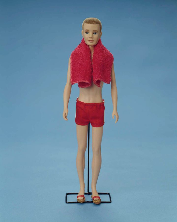 An original 1961 Ken doll wears a bathing suit and a towel in this studio portrait.