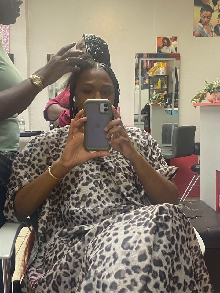 The author sitting in the braider's chair mid-install of her protective hairstyle.