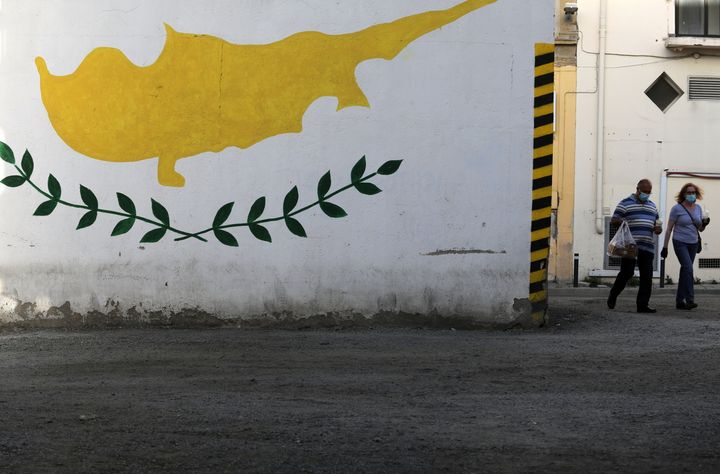 People wearing protective masks walk next to a Cypriot flag painted on a wall in capital Nicosia, Cyprus April 27, 2021. REUTERS/Yiannis Kourtoglou