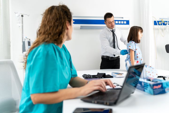Female Head Nurse and Professional Doctor Making Checkup on little girl Patient . They Talk, Check Computer for Vitals