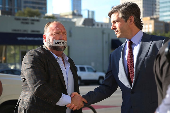 Alex Jones, shown shaking hands with his lawyer Andino Reynal, arrives at the Travis County Courthouse on July 26, 2022, with a piece of tape over his mouth that reads "Save the 1st."