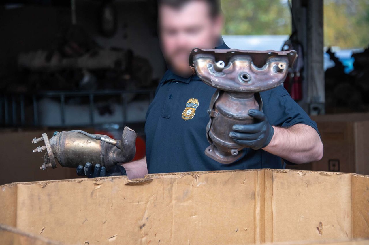 An officer with Homeland Security Investigations holds a stolen catalytic converter as part of a raid on illegal catalytic converter businesses in Operation Heavy Metal.