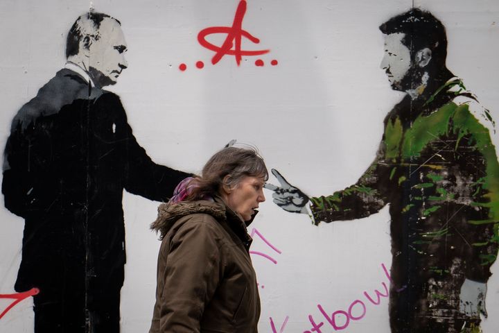 A woman walks by a graffiti depicting Ukrainian President Volodymyr Zelenskyy, right, and Russian President Vladimir Putin in central London, on May 4, 2023.