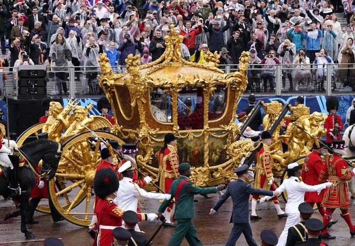 King Charles III and Queen Camilla are carried in the Gold State Coach, pulled by eight Windsor Greys, in the Coronation Procession.