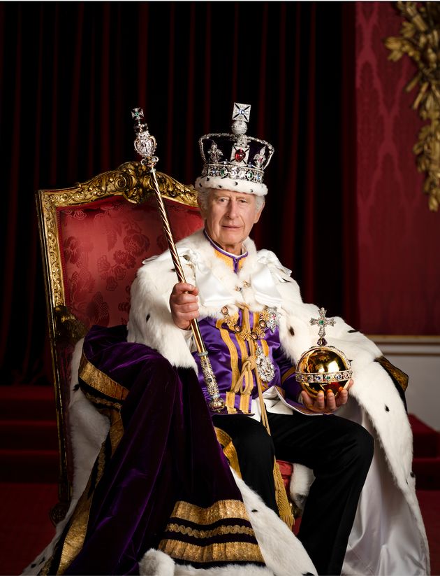 King Charles is pictured in full regalia in the Throne Room at Buckingham Palace, wearing the Robe of Estate and the Imperial State Crown while holding the Sovereign’s Orb and Sovereign’s Sceptre with Cross.