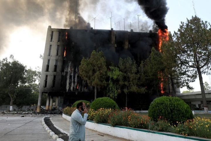 Ένας άντρας μιλάει στο κινητό του καθώς φωτιά και καπνός βγαίνουν από το κτίριο του Radio Pakistan μετά την πυρπόλησή του από τους υποστηρικτές του πρώην πρωθυπουργού Ιμραν Χαν κατά τη διάρκεια διαμαρτυρίας για τη σύλληψή του, στην Πεσαβάρ του Πακιστάν, 10 Μαΐου 2023.